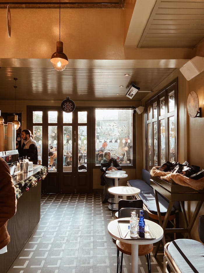 hero-img-02 Warm and inviting café interior with wooden furniture, large windows, and soft lighting.